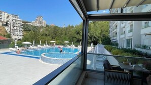 Un balcón con vistas a una piscina, sillas de descanso y un comedor.