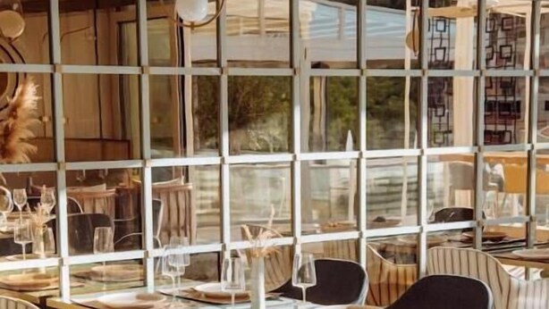 Un comedor con un ventanal grande, sillas a rayas y una mesa de vidrio.