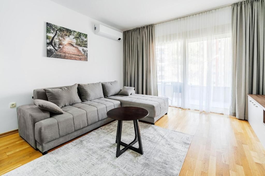 A modern living room with a grey sofa, a round coffee table, and a painting on the wall.