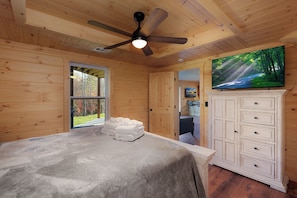 A bedroom with a bed, a ceiling fan, a TV, a wardrobe, and a window with a view of trees. - Peaches & Streams, Blue Ridge, GA (Morganton)