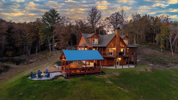 Eine große Holzhütte mit einer Terrasse und Sitzbereich im Freien, umgeben von Bäumen.