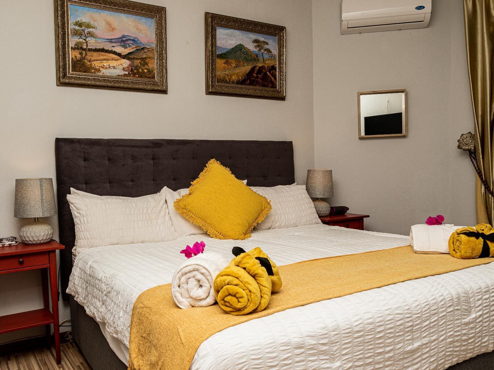 A hotel room with a bed, two paintings, a mirror, and a window with curtains.