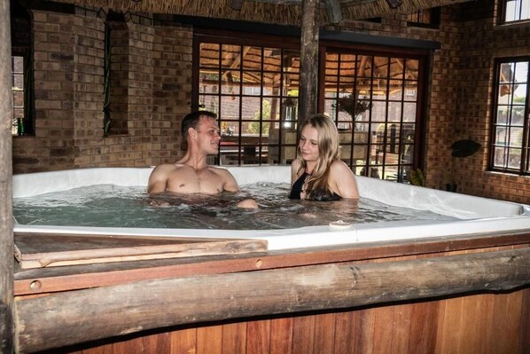 A wooden hot tub with a brick wall and windows in the background.