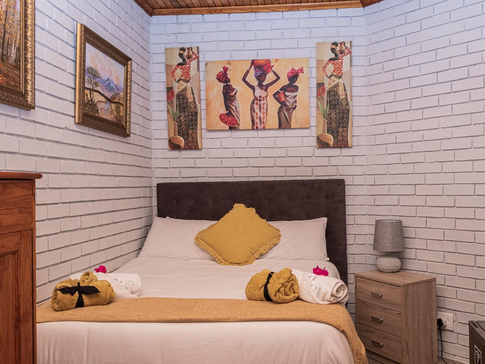Habitación de hotel con pared de ladrillo, cama con cabecero oscuro y cuadros en la pared.
