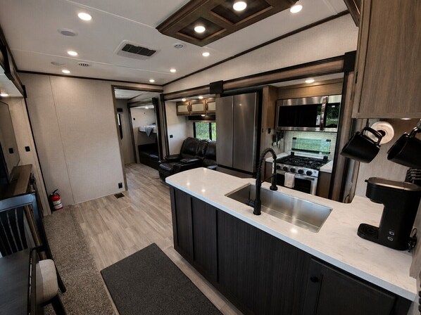 Une cuisine compacte pour camping-car, dotée d’un îlot central, d’appareils électroménagers en acier inoxydable et d’un coin repas avec une banquette.