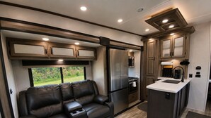 A compact RV interior with a sofa, kitchenette, and a view through a window. - The TajMyHaul, Camper in Waterside at Blue ridge! (Morganton)