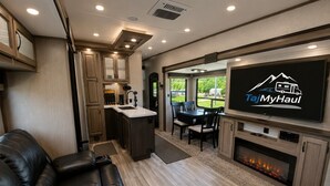 A compact RV interior with a kitchenette, a flat-screen TV, a leather couch, and a fireplace. - The TajMyHaul, Camper in Waterside at Blue ridge! (Morganton)