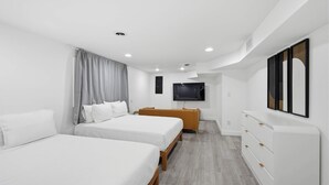 Una habitación de hotel moderna con dos camas, un televisor, un aparador de madera y una cortina gris.