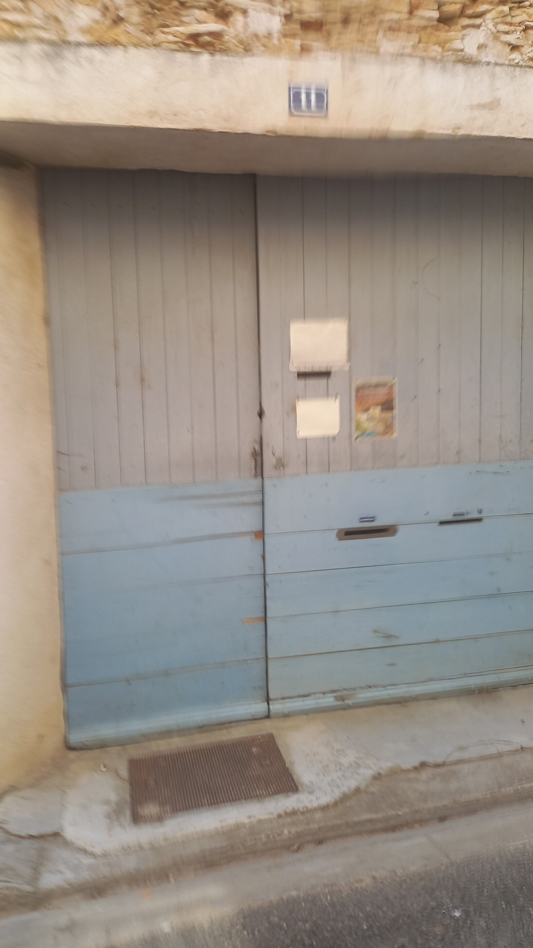 Puerta doble cerrada con un pequeño respiradero encima, una rejilla metálica en el suelo y una pared de textura rugosa.