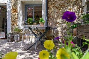 A stone building with a table and chairs outside, surrounded by potted plants and flowers. - Private Room 'l'habitant' (Villes-sur-Auzon)