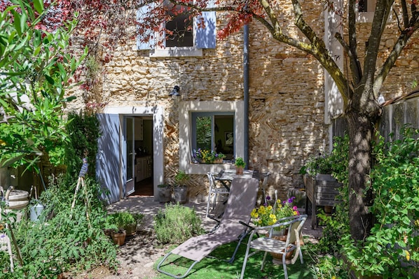 A stone building with a garden, outdoor seating, and a tree.