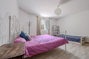 A bedroom with a bed, a small table, a radiator, and a window with curtains.