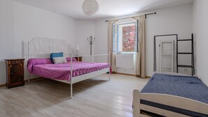 Een slaapkamer met een bed, een dressoir, een raam met gordijnen, een radiator en een trap.