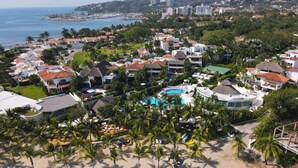 Um resort costeiro com vários edifícios, piscina e palmeiras.