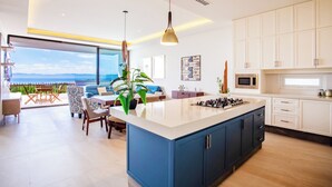 Uma cozinha moderna com ilha central, armários brancos e vista para o oceano.