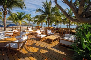 A wooden deck with outdoor seating, palm trees, and a view of the sea. - Jungle Hideaway · Private Pool & Beach Club (La Cruz de Huanacaxtle)