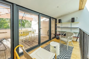 A modern room with a sliding glass door leading to an outdoor patio, a white wicker chair, a small table, and a fan on the floor.