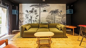 En moderne stue med sofa, lille bord og et mural med tropiske planter.