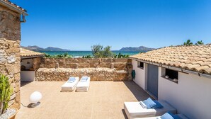 A terrace with stone walls, a view of the sea, and lounge chairs. - Finca in front of the sea, Can Cuarassa, Pollensa. (Pollensa)