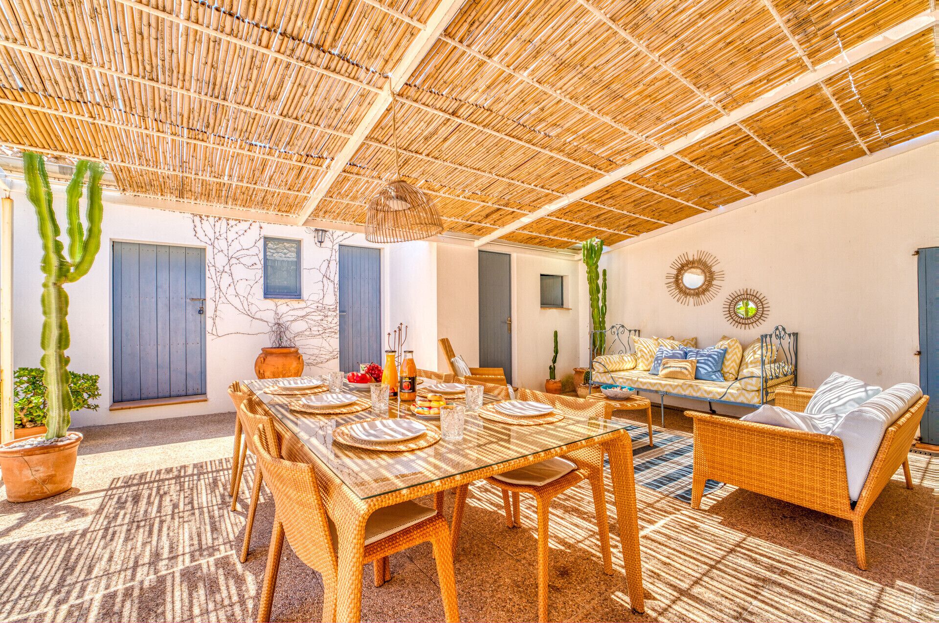 A spacious outdoor dining area with a bamboo ceiling, wicker furniture, and potted plants.
