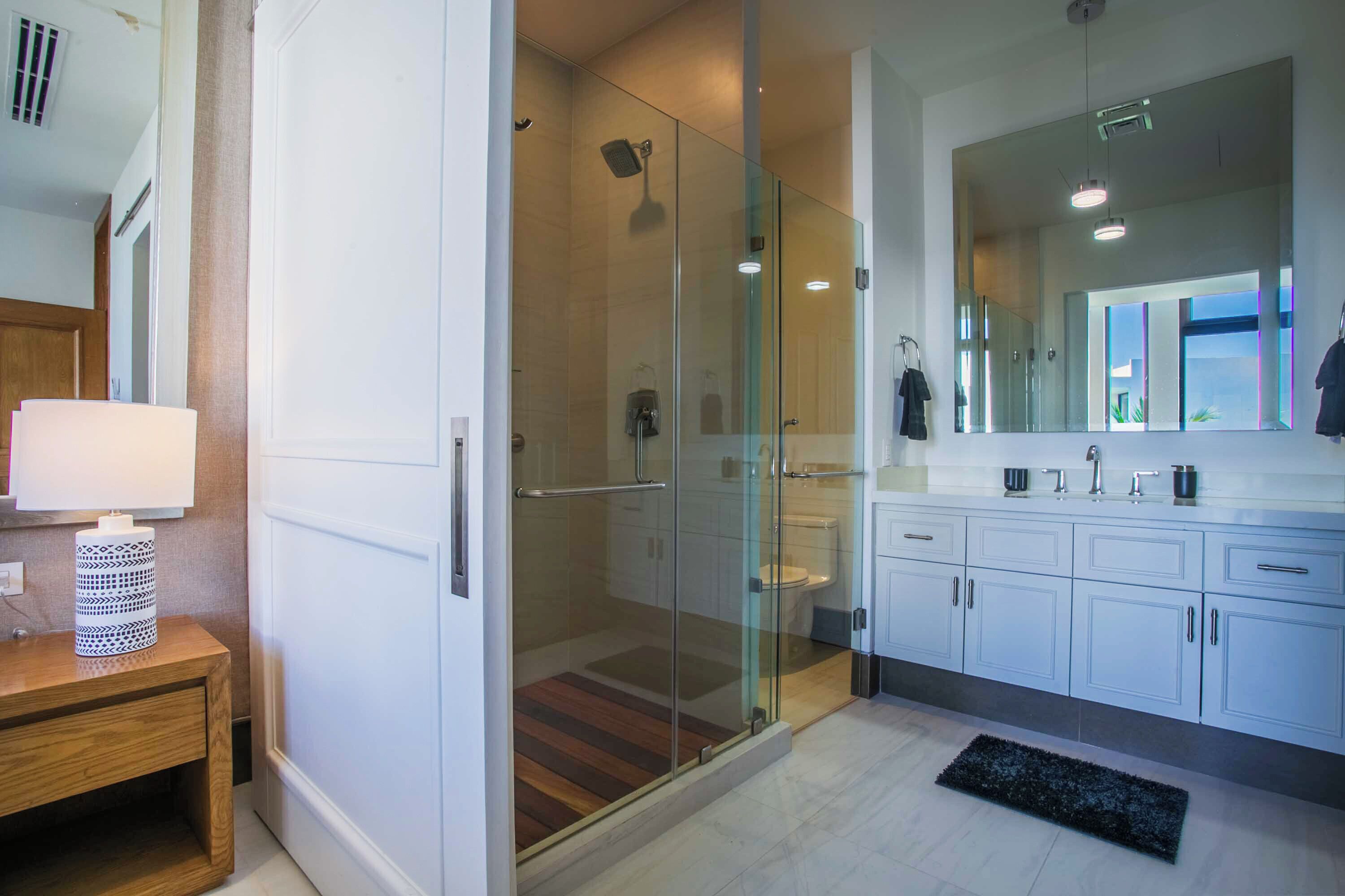 A modern bathroom with a glass-enclosed shower, a large mirror, and white cabinetry.