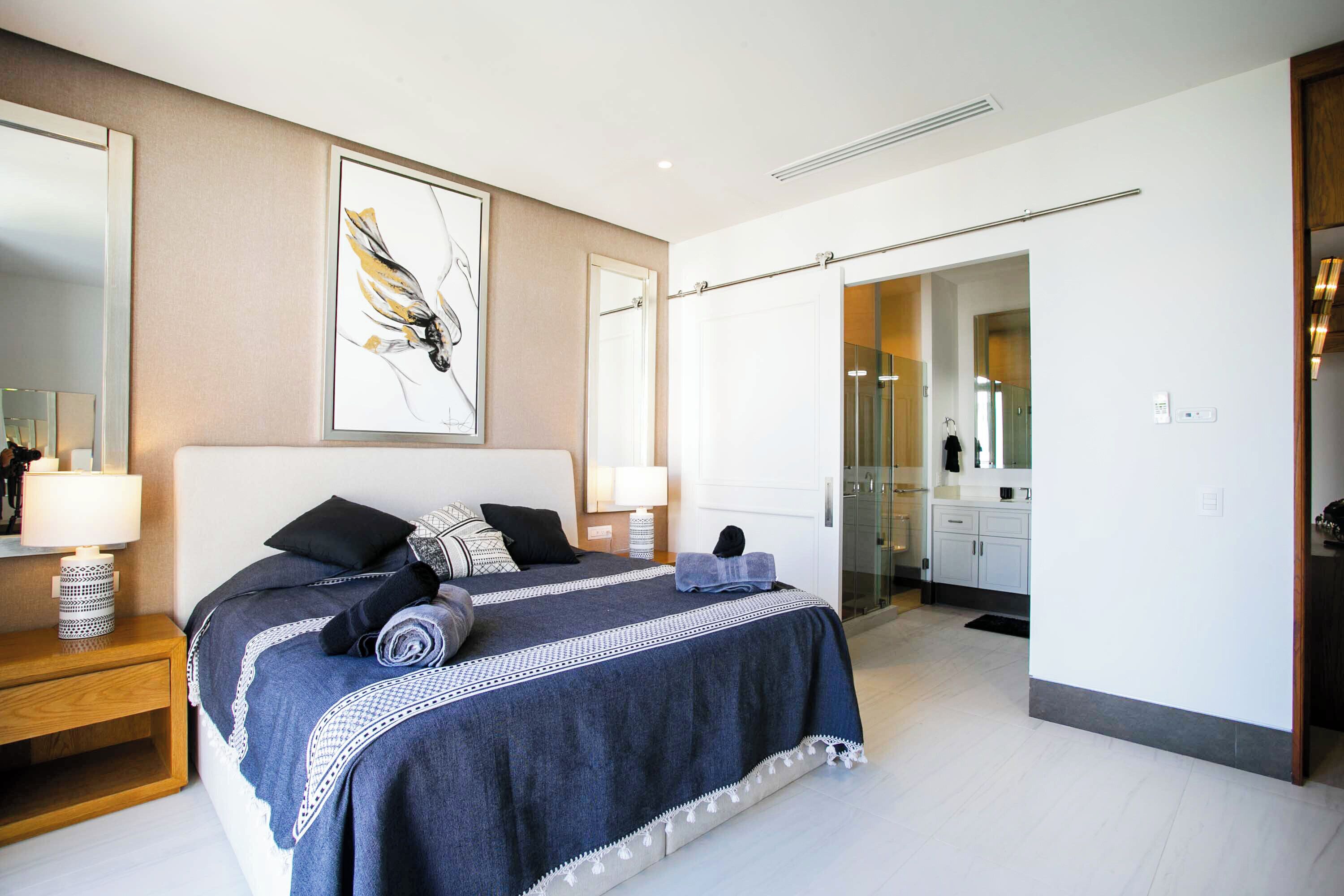 Un dormitorio moderno con una cama grande, lámparas de noche, un espejo y un baño visible a través de una puerta abierta.