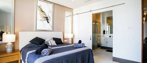 Un dormitorio moderno con una cama grande, lámparas de noche, un espejo y un baño visible a través de una puerta abierta.