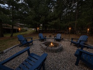 An outdoor seating area with Adirondack chairs and a fire pit surrounded by gravel.