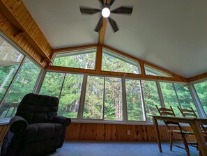A room with large windows, a ceiling fan, a dark armchair, and a wooden table.