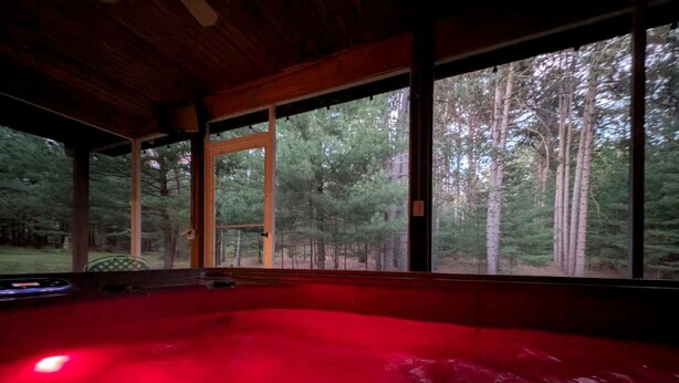 Ein Whirlpool mit roter Beleuchtung, großen Fenstern und Blick auf einen Wald.