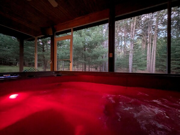 A hot tub with a red light, large windows, and a view of a forest.