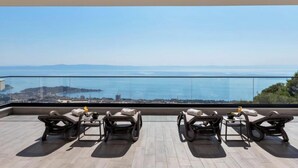 A rooftop terrace with four lounge chairs, a small table, and a view of the sea and cityscape. - Villa Basak (Makarska)