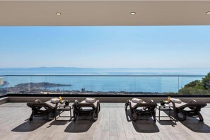 A rooftop terrace with four lounge chairs, a small table, and a view of the sea and cityscape. - Villa Basak (Makarska)
