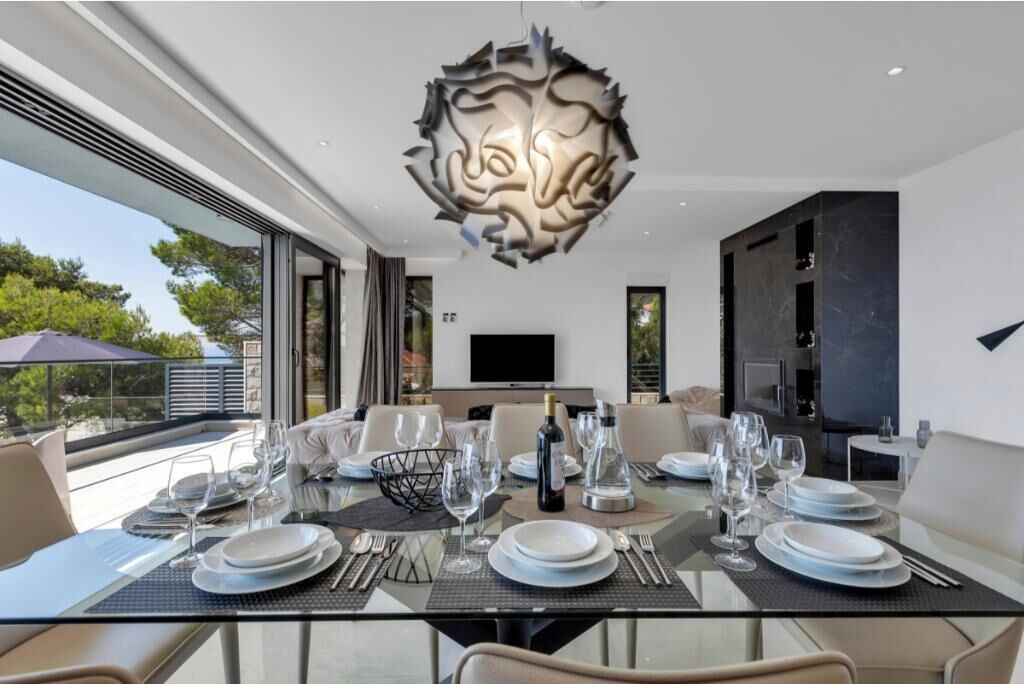 Uma área de refeições moderna com uma mesa de vidro, cadeiras de metal e uma escultura única no teto.
