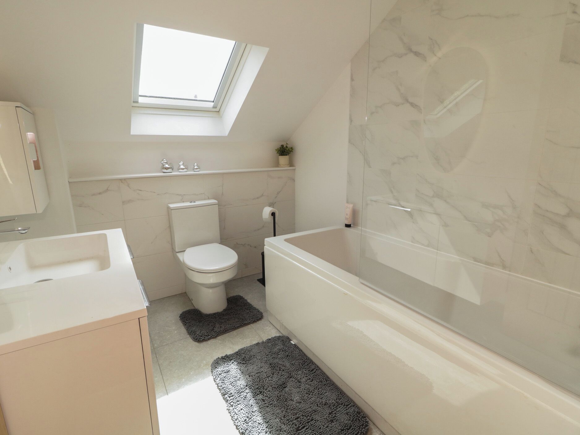 A bathroom with a skylight, a toilet, a bathtub, and a sink.
