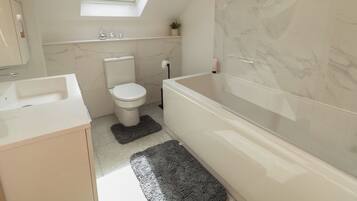 A bathroom with a skylight, a toilet, a bathtub, and a sink.