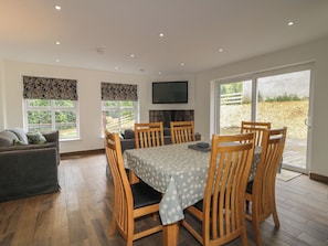 A dining area with a table, chairs, a sofa, and a TV on the wall. - Brook Cottage (Coleraine)