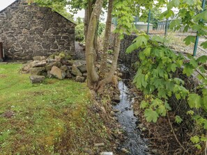 Un edificio de piedra, un árbol y un pequeño arroyo en un jardín.