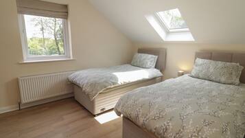 A bedroom with two beds, a skylight, a radiator, and a window with a view of trees.