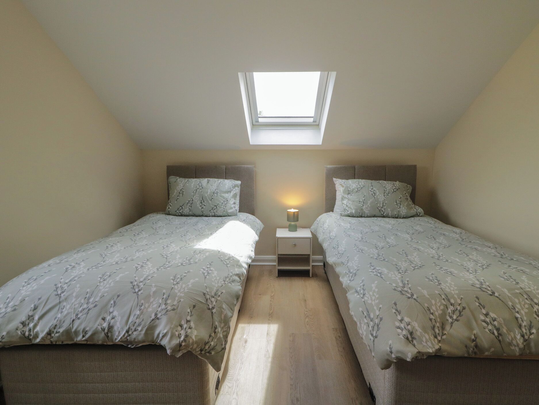A bedroom with two beds, a skylight, and a bedside table with a lamp.