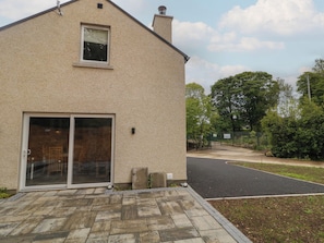 A beige building with a large sliding glass door, a small window, and a paved driveway leading to a road. - Brook Cottage (Coleraine)