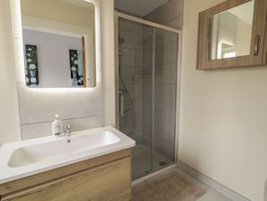 A bathroom with a white sink, wooden vanity, a glass shower enclosure, and a mirror with a wooden frame. - Brook Cottage (Coleraine)