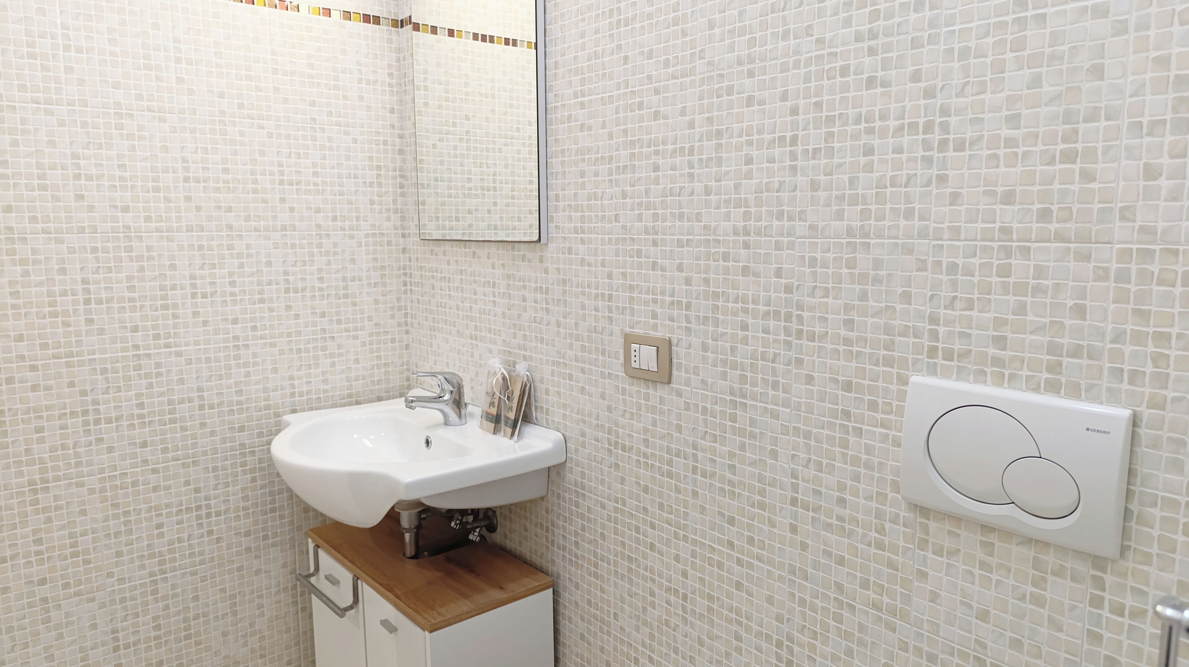 Ein Badezimmer mit einem weißen Waschbecken, einem Spiegel und einem Lichtschalter an der Wand.