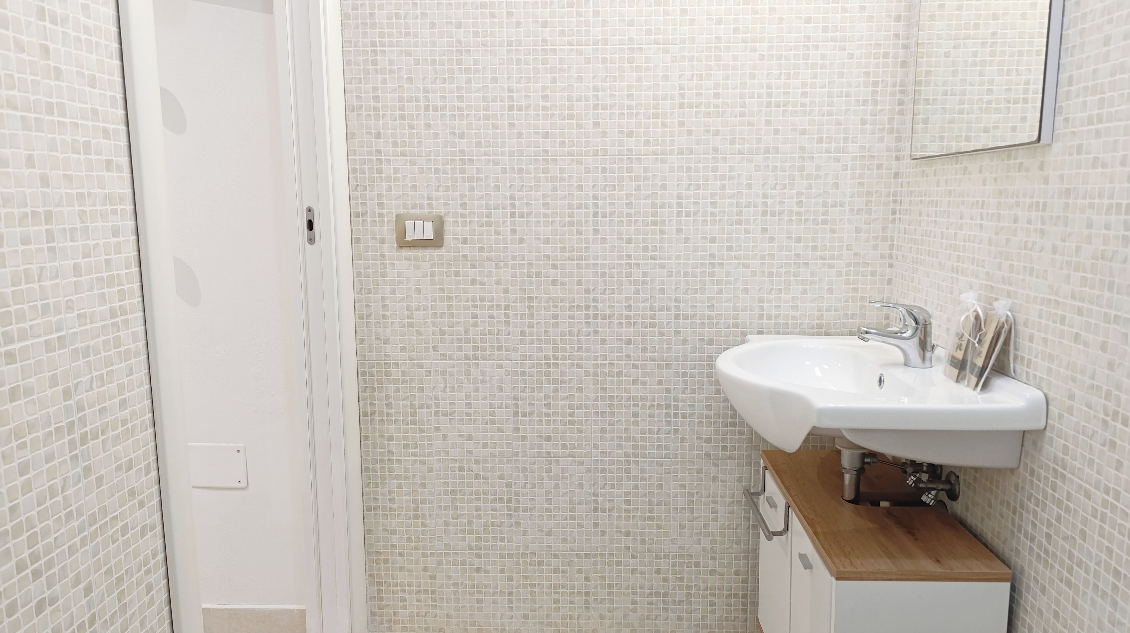 Une salle de bain avec un lavabo blanc, une douche et un mur recouvert de carreaux.