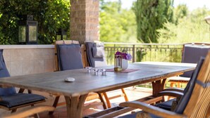 Een terras buiten met een houten tafel, stoelen en een vaas met bloemen.