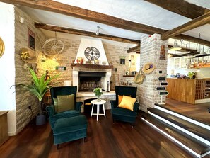 A cozy living room with a fireplace, two green armchairs, a small table with a vase, and a kitchen area in the background. - Villa Experience with swimming pool (Baderna)