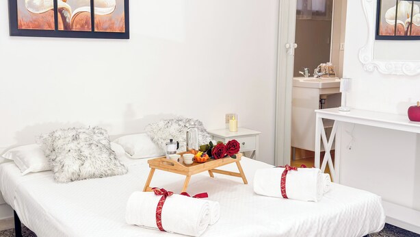 A neatly made bed with fluffy pillows, a bedside table with a candle, a tray with flowers and a tea set, and a mirror above the sink. - Cà 4 Nevodi Nonna Chiara Destro by Ca-Sa Check (Chioggia)