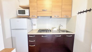 A compact kitchen with a refrigerator, microwave, gas stove, sink, and wooden cabinets. - Cà 4 Nevodi Nonna Chiara Destro by Ca-Sa Check (Chioggia)