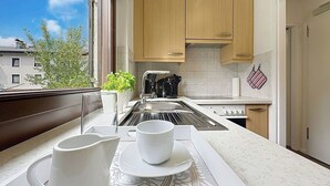 Une cuisine moderne avec des meubles en bois, un évier en acier inoxydable et une fenêtre donnant sur un immeuble.