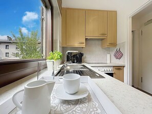 Eine moderne Küche mit Holzschränken, einer Edelstahl-Spüle und einem Fenster mit Blick auf ein Gebäude.
